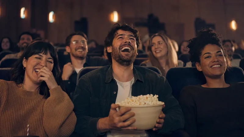 Skupina divákov sa smeje počas komédie v kine a muž v strede drží misku s popcornom