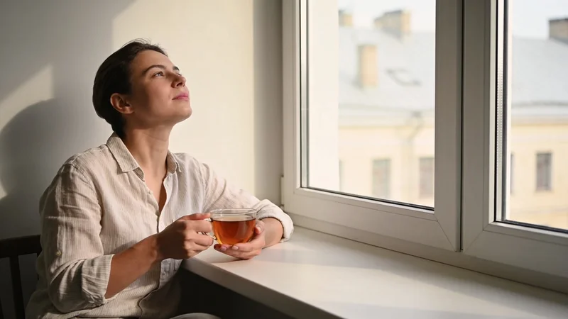 Človek pri okne premýšľa nad správou v telefóne pri rannom svetle