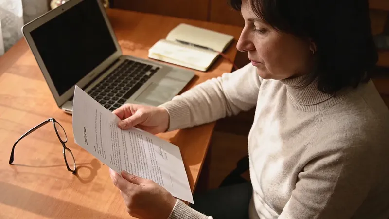 Opatrovateľka pri stole s dokumentmi a notebookom pripravuje zmluvu