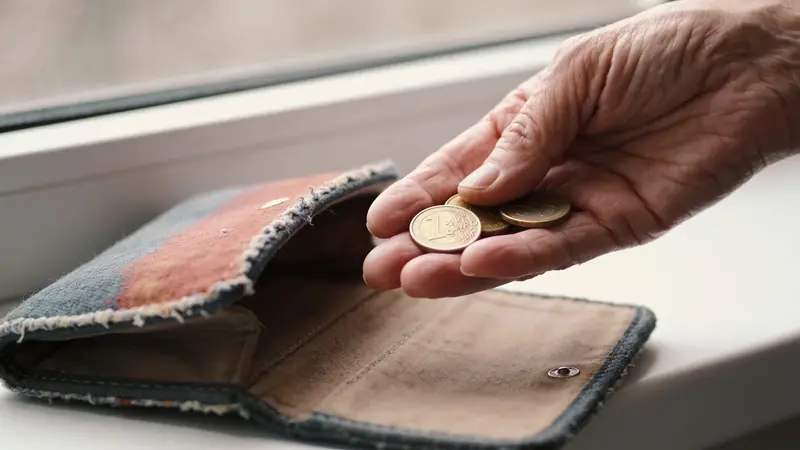 Ruka drží pár drobných mincí nad prázdnym vreckom