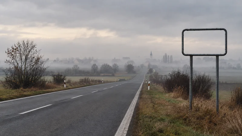 Prázdna cesta na Záhorí smeruje do hmly popri ráme bez obecnej tabule