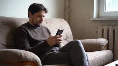 Človek sediaci doma na gauči a pozerajúci do smartfónu pri riešení zmeny operátora