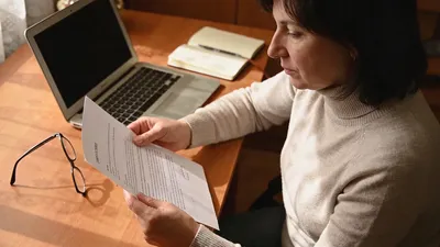Opatrovateľka pri stole s dokumentmi a notebookom pripravuje zmluvu