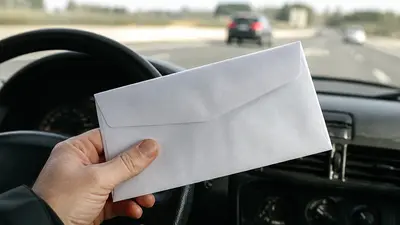 Ruka drží bielu úradnú obálku v aute na diaľnici