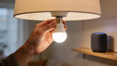 Ruka skrutkuje smart žiarovku, v pozadí smart reproduktor