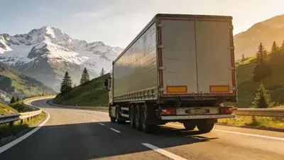 Vodič kamiónu v kabíne moderného európskeho ťahača s rukami na volante a alpskou cestou v pozadí