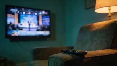 Televízna obrazovka so živým vysielaním v tmavej obývačke, na stolíku diaľkový ovládač